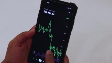 Woman looking through BTC 12 Hours chart on Black smartphone
