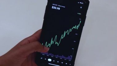 Woman looking through LINK 12 hours chart on Black smartphone