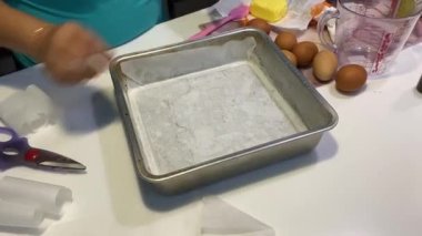 Kadın tereyağı ve pasta kağıdıyla kare pasta tepsisi diziyor 