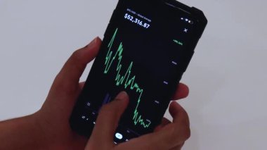 Woman looking through BTC 1 Year chart on Black smartphone