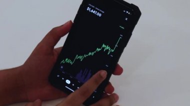 Woman looking through ETH 12 hours chart on Black smartphone