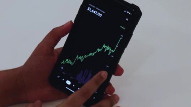 Woman looking through ETH 12 hours chart on Black smartphone