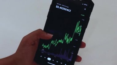 Woman looking through XRP 12 hours chart on Black smartphone.