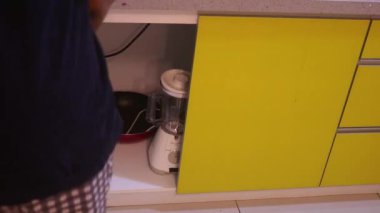 Ethnic Woman Getting Blender From A Cupboard