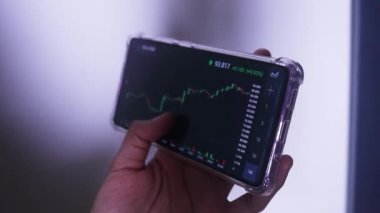 Woman Holding Phone In Landscape Mode Checking Solana's Hourly Chart