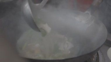 Çinli aşçı, içindekileri tavada karıştırıyor.