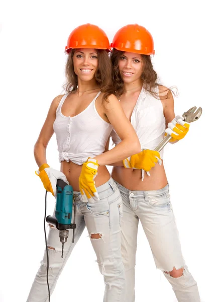 Chicas Géminis en cascos naranjas con taladro eléctrico y sierra eléctrica sobre fondo blanco . —  Fotos de Stock