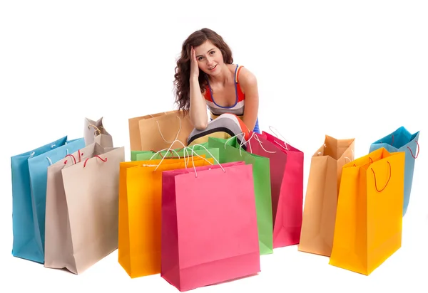 Uma menina em uma cor de vestido longo sentado ao lado de um saco de compras em um fundo branco . — Fotografia de Stock