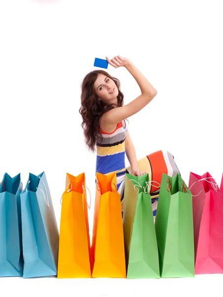 Mujer en vestido largo de color, de pie junto a una bolsa de compras con una tarjeta de crédito sobre un fondo blanco . —  Fotos de Stock