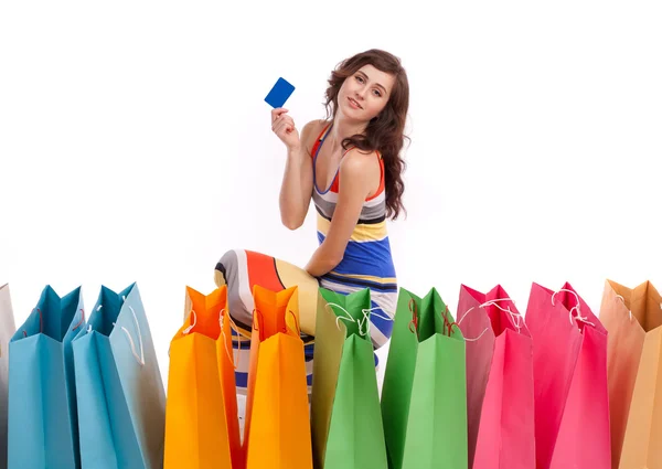 Mulher de vestido longo colorido, de pé ao lado de um saco de compras com um cartão de crédito em um fundo branco . — Fotografia de Stock