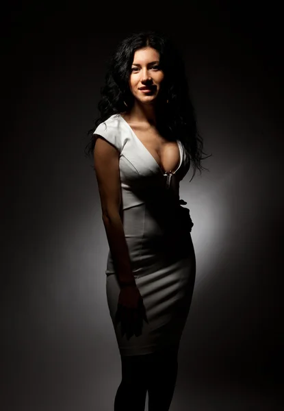 Vacker brunett med stora bröst i en vit klänning på en mörk bakgrund. — Stockfoto