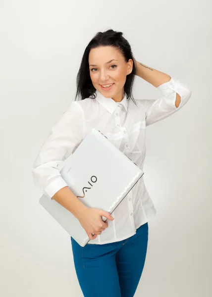 Hermosa chica en una camisa blanca y vaqueros azules con un ordenador portátil sobre un fondo gris —  Fotos de Stock