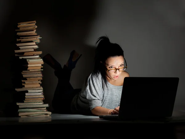 Bella studentessa sdraiata sul pavimento con laptop e libri su uno sfondo scuro — Foto Stock