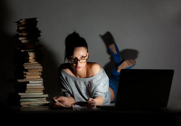 Bella studentessa sdraiata sul pavimento con laptop e libri su uno sfondo scuro — Foto Stock