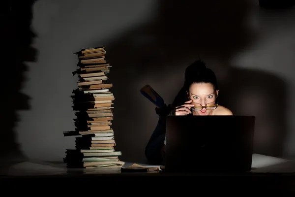 Schöne Studentin auf dem Boden liegend mit Laptop und Büchern auf dunklem Hintergrund — Stockfoto