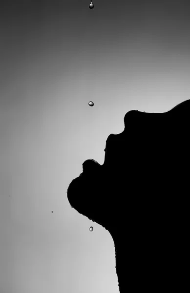 Silhouette di una ragazza in bocca dove una goccia d'acqua cade su uno sfondo scuro Foto Stock