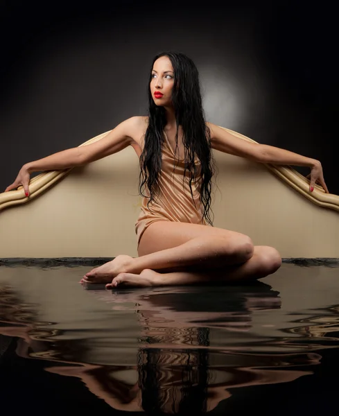 Chica con el pelo mojado y ropa mojada sentada en el agua negra sobre un fondo negro — Foto de Stock