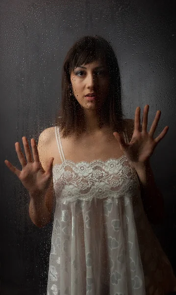 De brunette in een witte jurk voor een natte glas op een zwarte achtergrond. — Stockfoto