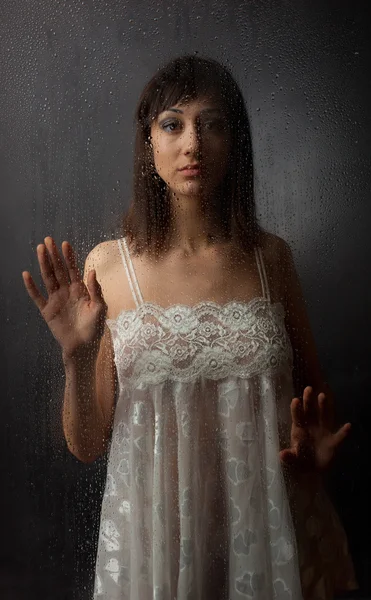 De brunette in een witte jurk voor een natte glas op een zwarte achtergrond. — Stockfoto