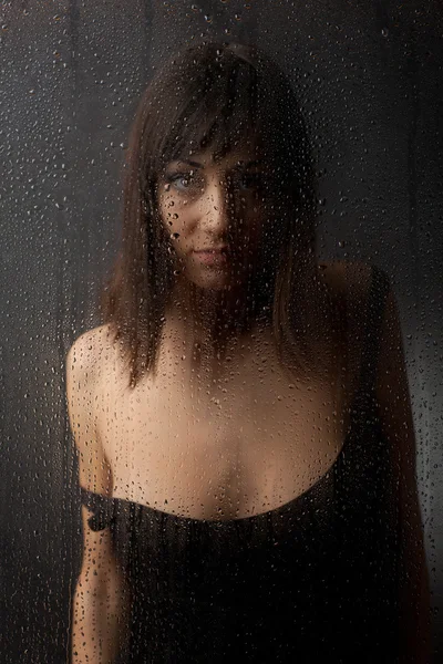 The brunette in a black dress for a wet glass on a black background. — Stock Photo, Image