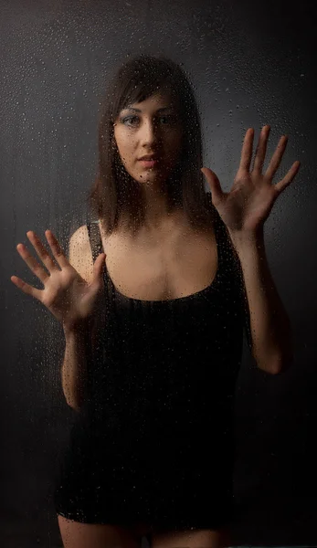 Brunett i en svart klänning för en våt glas på svart bakgrund. — Stockfoto