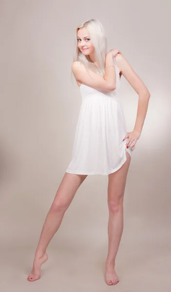 Gri bir arka plan üzerinde kısa beyaz elbiseli güzel yalınayak kız — Stok fotoğraf