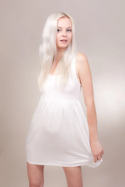 Hermosa chica en un vestido blanco corto sobre un fondo gris — Foto de Stock