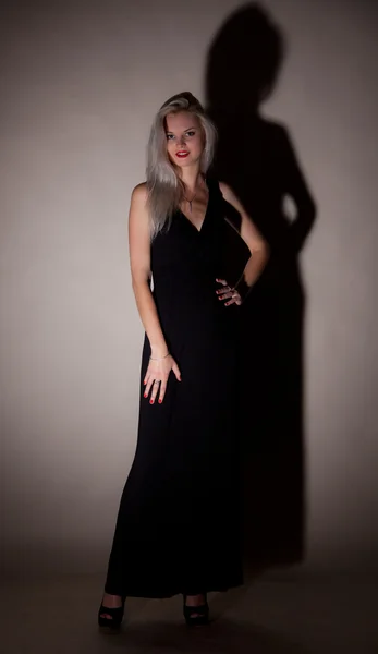 एक राखाडी पार्श्वभूमी वर एक लांब काळा ड्रेस मध्ये सुंदर मुलगी — स्टॉक फोटो, इमेज