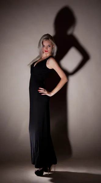 Beautiful girl in a long black dress on a gray background — Stock Photo, Image