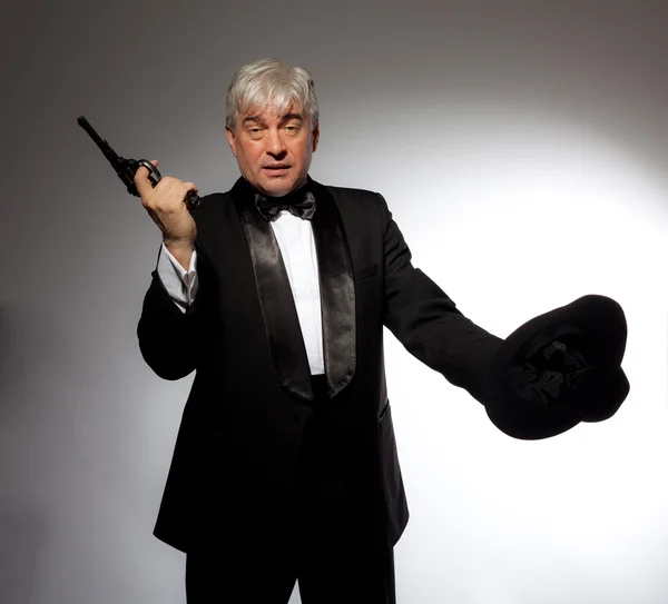 El hombre elegante en esmoquin con sombrero y pistola sobre fondo gris — Foto de Stock