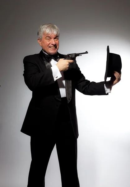 The elegant man in a tuxedo with a hat and a gun on a gray background — Stock Photo, Image