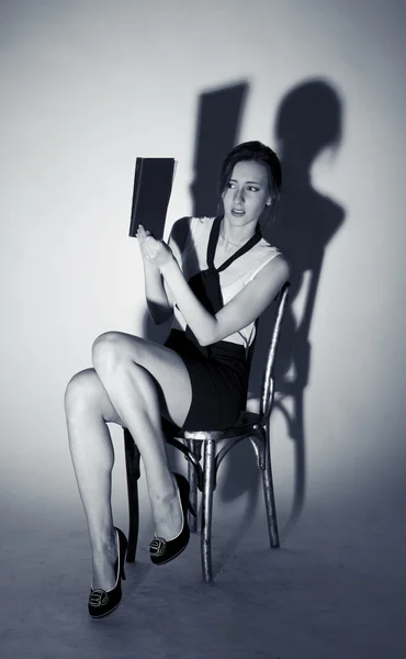 Dívka sedí na židli a čtení hroznou knihu — Stock fotografie