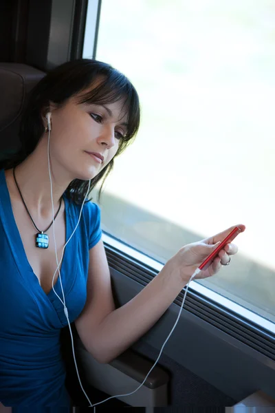 Beautiful young woman dreaming in a train listening to music on a mp3 player ipod type — Stock Photo, Image