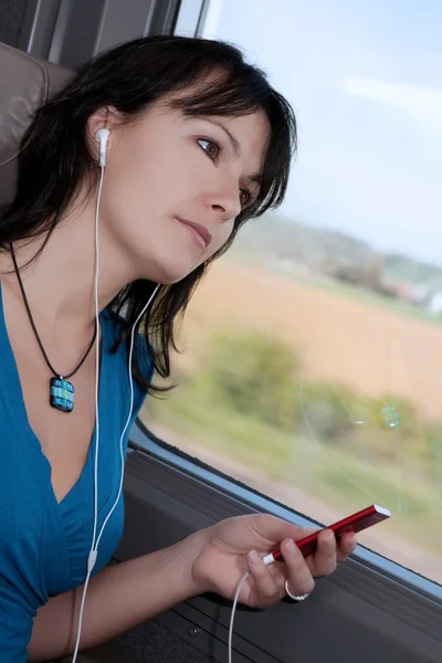Beautiful young woman dreaming in a train listening to music on a mp3 player ipod type — Stock Photo, Image
