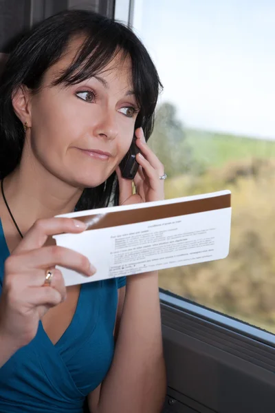 Vacker ung kvinna i ett tåg att göra ett telefonsamtal med en biljett i handen — Stockfoto