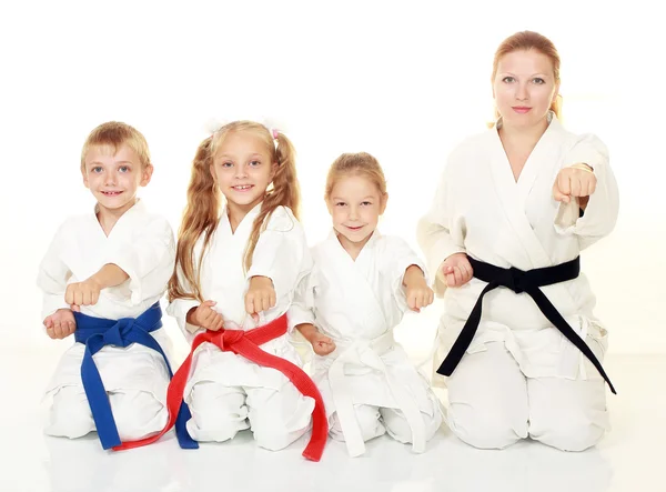 Mamá con su hija y un niño sentado con su hermana en un ritual pose karate y golpeó su puño —  Fotos de Stock