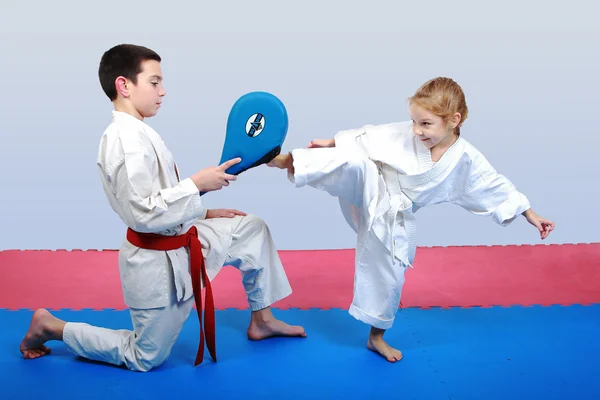 Petite fille avec une ceinture blanche battent jambe sur le simulateur dans les mains d'un garçon avec une ceinture rougePetite fille avec une ceinture blanche battent jambe sur le simulateur dans les mains d'un garçon avec une ceinture rouge — Photo