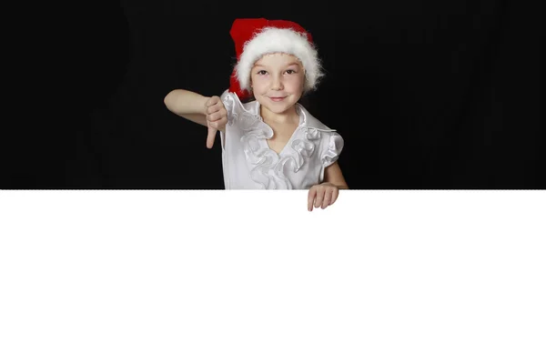 A menina no chapéu Papai Noel mostra o dedo em um cartaz — Fotografia de Stock