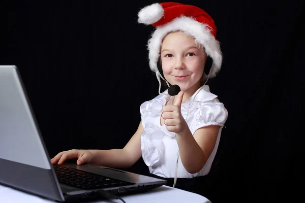 Am computer sitzt ein kleines mädchen mit mütze von weihnachtsmann — Stockfoto