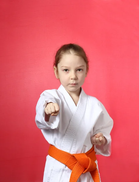 Girl on a red background with an orange belt is hitting right hand — Stock Photo, Image