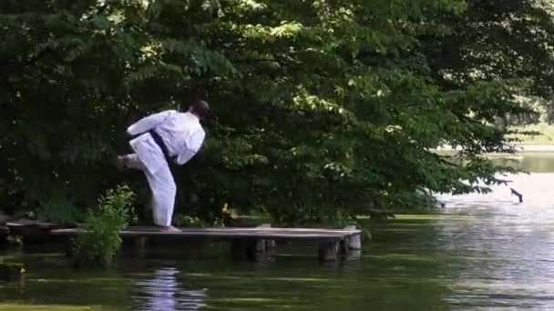 一名男子运动员在一个池塘的背景下在桥上训练向前和向后的踢腿 — 图库视频影像
