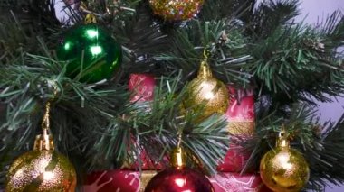 Yeşil bir Noel ağacındaki video kartpostallı Noel oyuncakları ve arka planda kırmızı paketlenmiş hediyeler.
