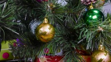 Yeşil bir Noel ağacında video kartpostallı Noel oyuncakları ve açık mavi arka planda kırmızı paketlenmiş hediyeler.