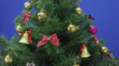 Hediyenin yanında güzel dekore edilmiş büyük yeşil bir Noel ağacı mavi bir arka planda dönüyor.