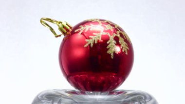 Altın kar taneleriyle süslenmiş kırmızı top hafif bir zemin üzerinde döner