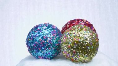 Yıldızlarda üç tane renkli Noel topu beyaz bir yüzey üzerinde yatar ve döner.