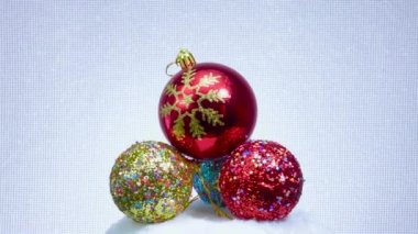 Kar taneli kırmızı top ve yıldızlarla süslenmiş üç top beyaz bir yüzey üzerinde döner.