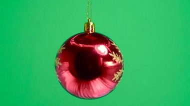 Yeşil bir arka planda, kar tanesiyle süslenmiş kırmızı bir top dönüyor.