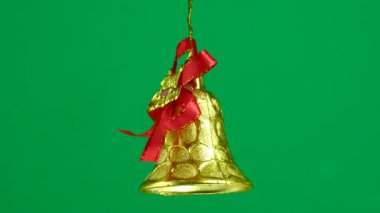Altın bir Noel oyuncak çanı yeşil bir arka planda dönüyor.