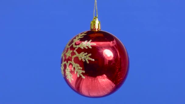 赤いクリスマスのおもちゃのボールが青いしっかりとした背景で回転しています — ストック動画